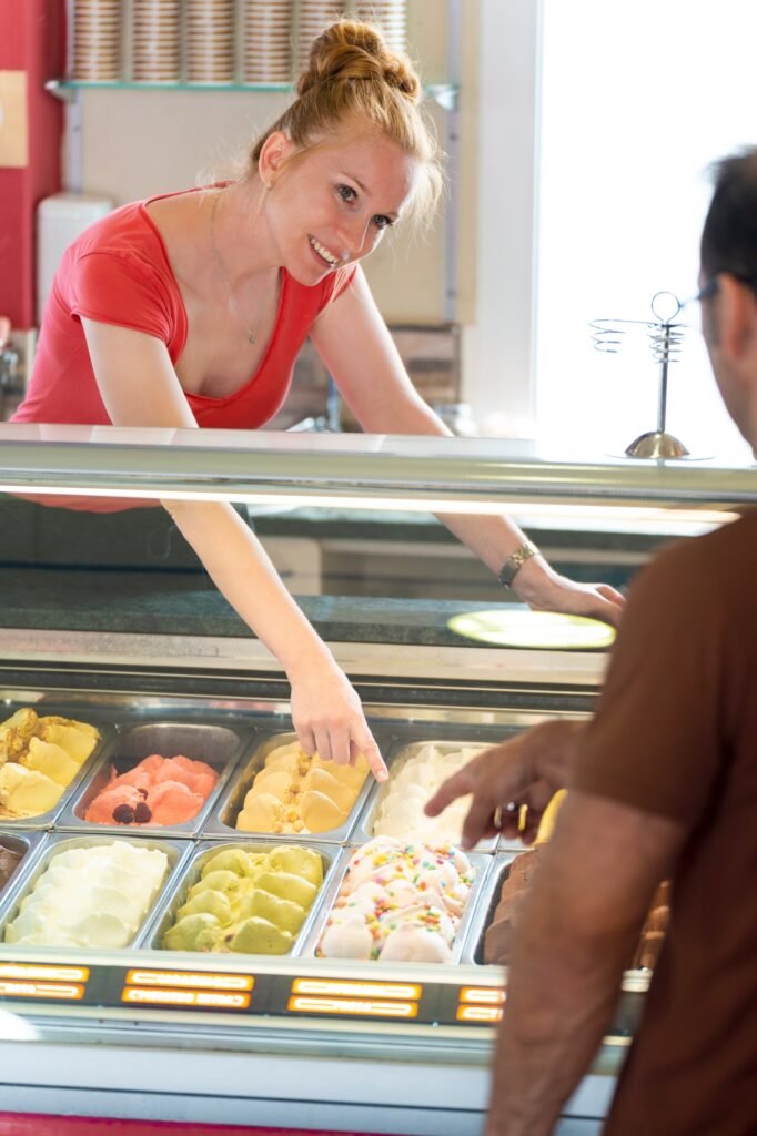 Man choosing a flavor of ice cream in a store with a female assistant
